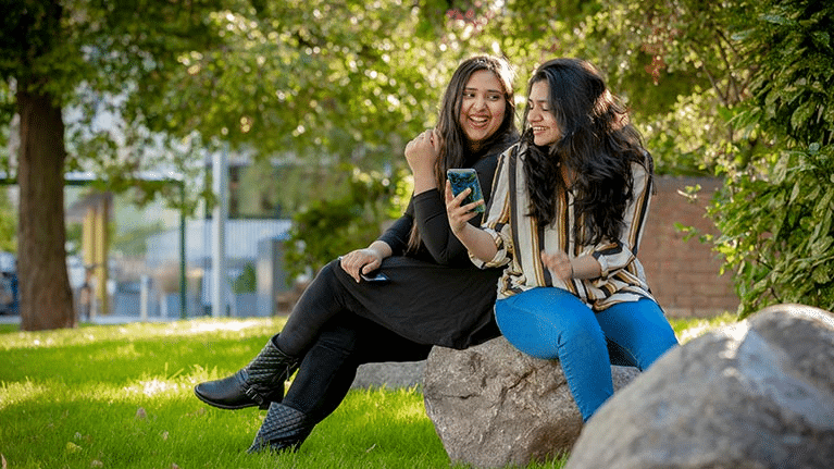 two women sitting on a rock smiling, university students sexual health