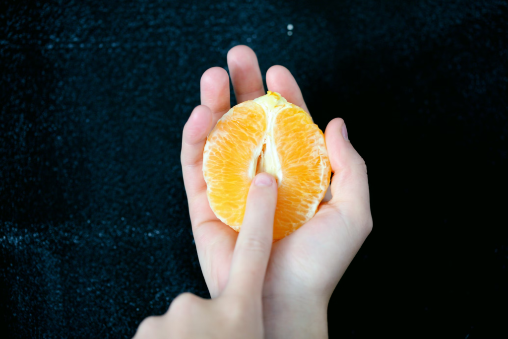 hand holding half and orange and using finger in a suggestive way, sexual health