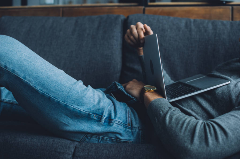 Alt: Man laying on the couch reaching into his pants with a laptop resting on his chest/mid section.