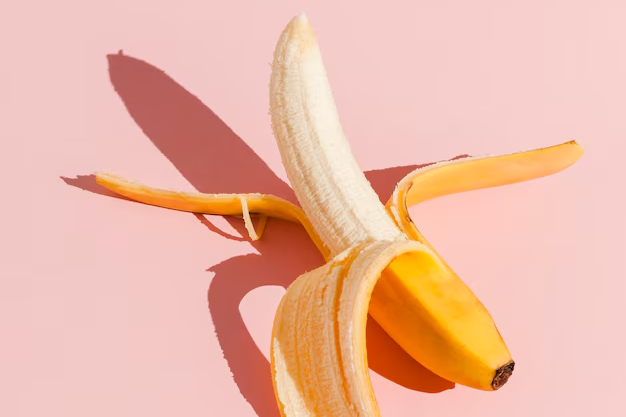 Alt: Seductive photo of a banana laying on a pink table, representing a penis