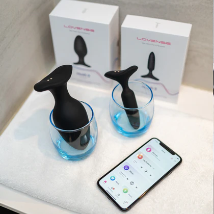 Two of Lovense's Hush 2's in cups with a cellphone next to them showing the Remote app