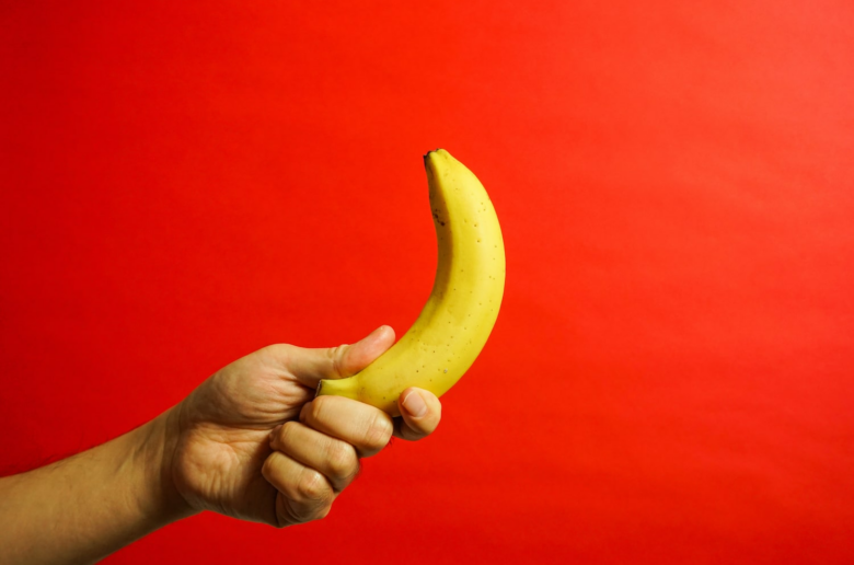 hand holding a banana over an orange background
