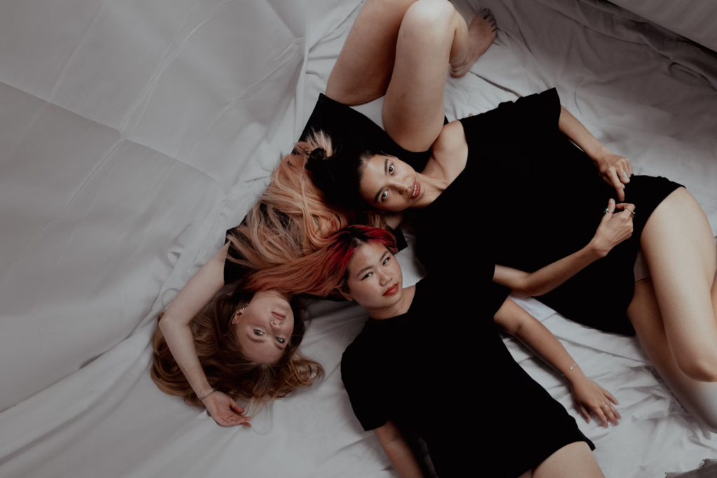 Three women lying together on a bed representing threesome intimacy