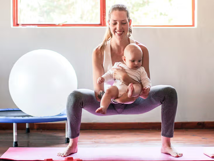 Mother squatting while holding a baby as she does pelvic floor strengthening exercises